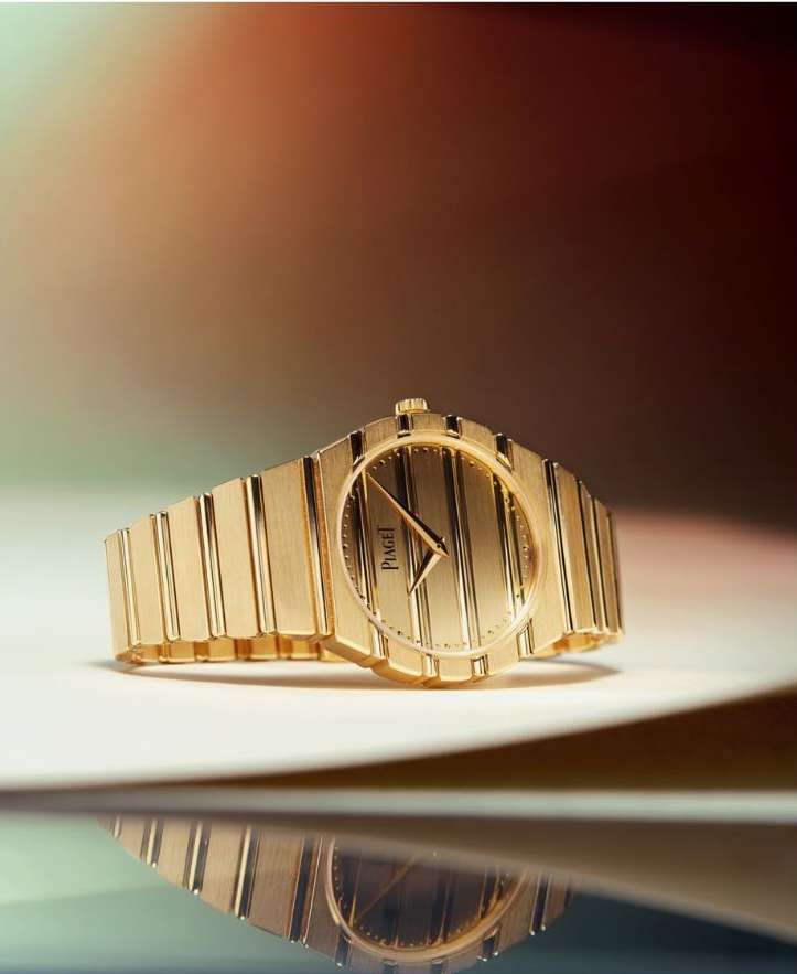 Close-up shot of a luxurious gold Piaget watch with vertical stripes on its face, positioned on a reflective surface.