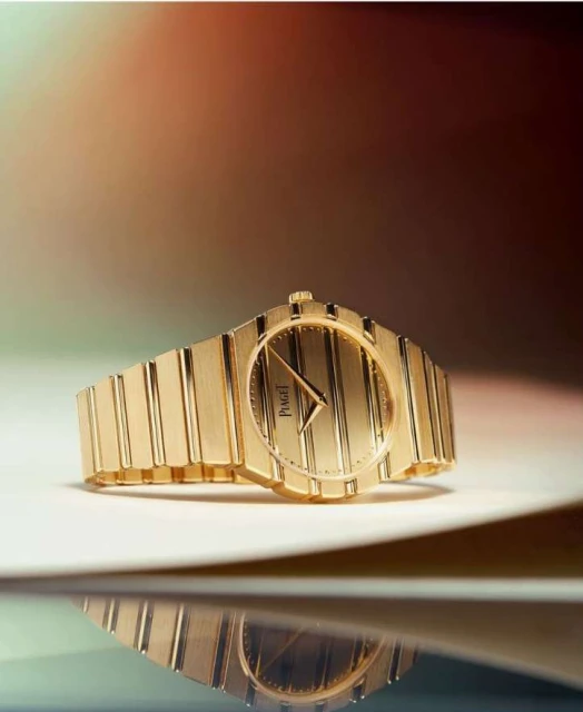 Close-up shot of a luxurious gold Piaget watch with vertical stripes on its face, positioned on a reflective surface.