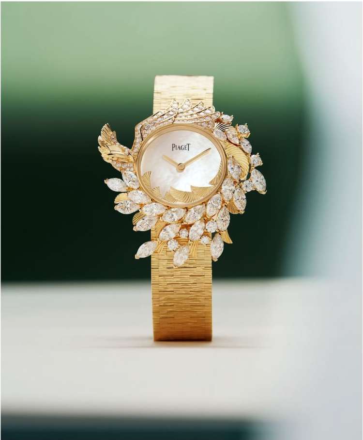 Elegant gold Piaget wristwatch with white mother-of-pearl dial and diamond leaf embellishments, showcased against a green gradient backdrop.