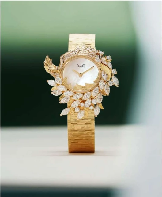 Elegant gold Piaget wristwatch with white mother-of-pearl dial and diamond leaf embellishments, showcased against a green gradient backdrop.