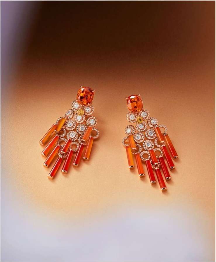 Two orange gemstone earrings with dangling accents are displayed against an orange gradient background in this jewelry advertisement.