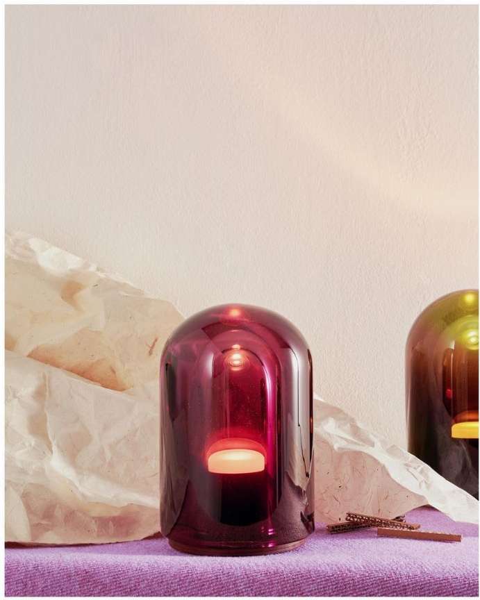 Illuminated purple glass dome light with a peach-colored glow, set against a light background with crumpled paper and a purple surface.