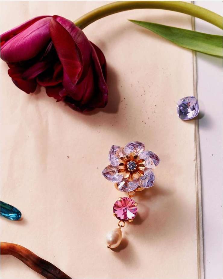 A close-up still life of a burgundy tulip, flower-shaped earrings, and gems on a cream surface, creating an elegant and floral-themed composition.