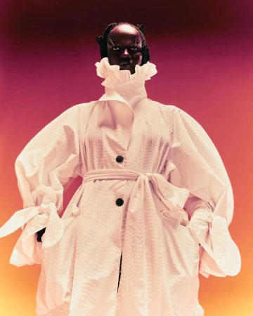Black woman wearing a textured white coat with ruffled collar against a gradient red and yellow background