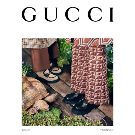 Gucci fashion campaign featuring two women wearing Gucci loafers, one with patterned pants, next to a tortoise on a wooden path.