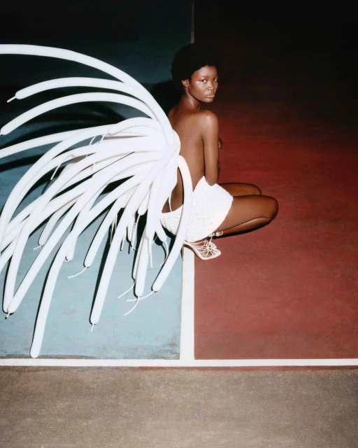 Striking image features an African-American woman in light-colored apparel with a 'wing' of white balloons, posing on a red and blue split background.