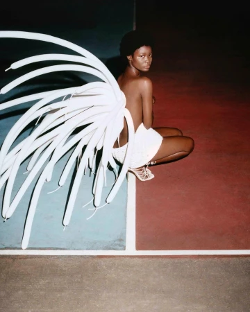 Striking image features an African-American woman in light-colored apparel with a 'wing' of white balloons, posing on a red and blue split background.