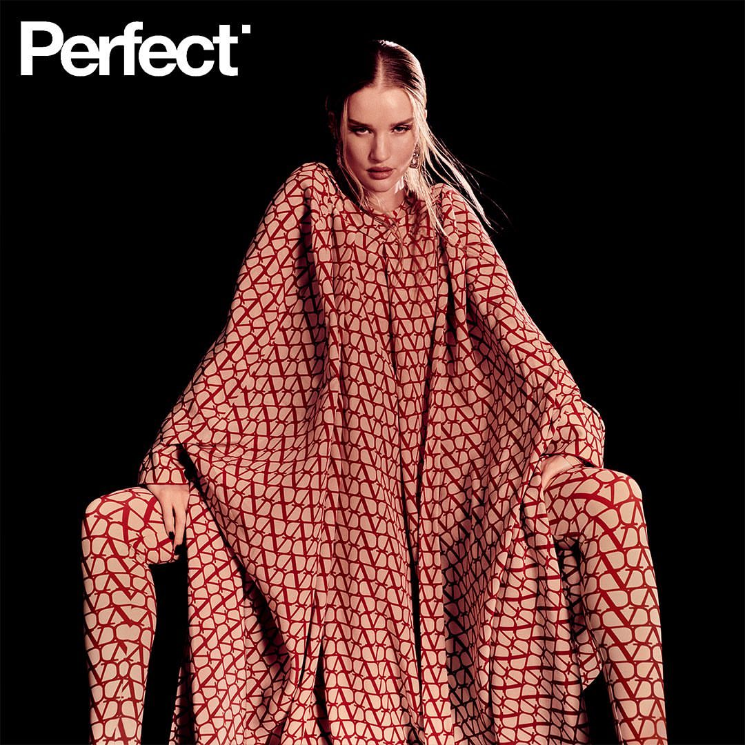 Fashion editorial shot of a woman in patterned red and beige matching tunic and leggings, posing against a dark background in studio lighting.