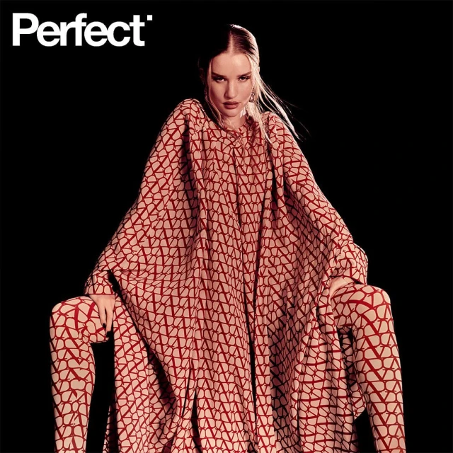 Fashion editorial shot of a woman in patterned red and beige matching tunic and leggings, posing against a dark background in studio lighting.