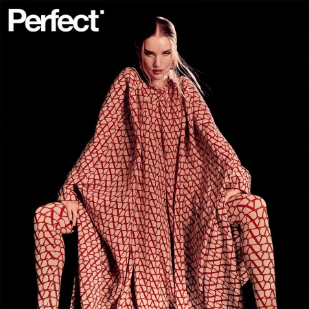Fashion editorial shot of a woman in patterned red and beige matching tunic and leggings, posing against a dark background in studio lighting.