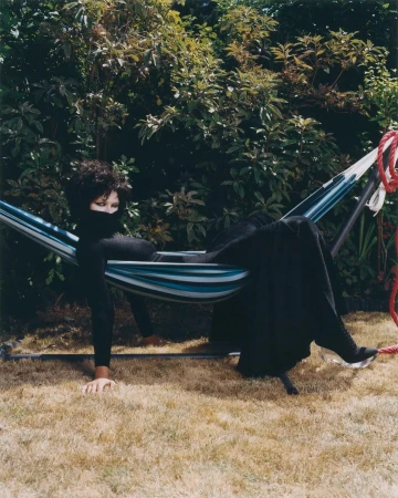 Model in black clothing lying in a striped hammock outdoors in a garden by photographer Amber Pinkerton