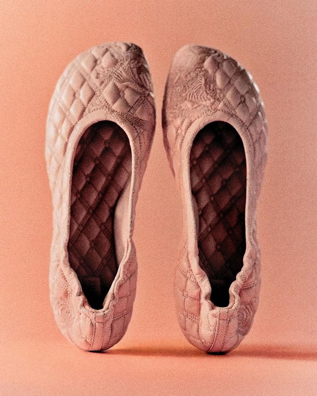 Two quilted, light-pink ballet flats displayed side by side on a pale-pink background in a close-up studio shot.