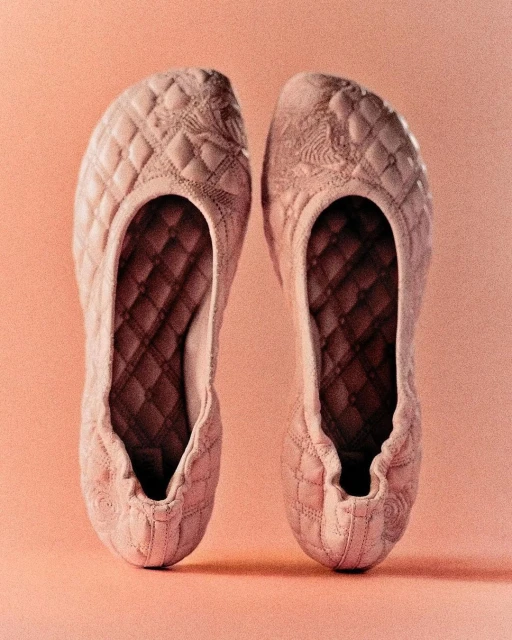 Two quilted, light-pink ballet flats displayed side by side on a pale-pink background in a close-up studio shot. 