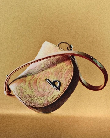 Close-up of a pink and gold patterned saddlebag purse with a silver clasp, on a monochromatic gold background for fashion.