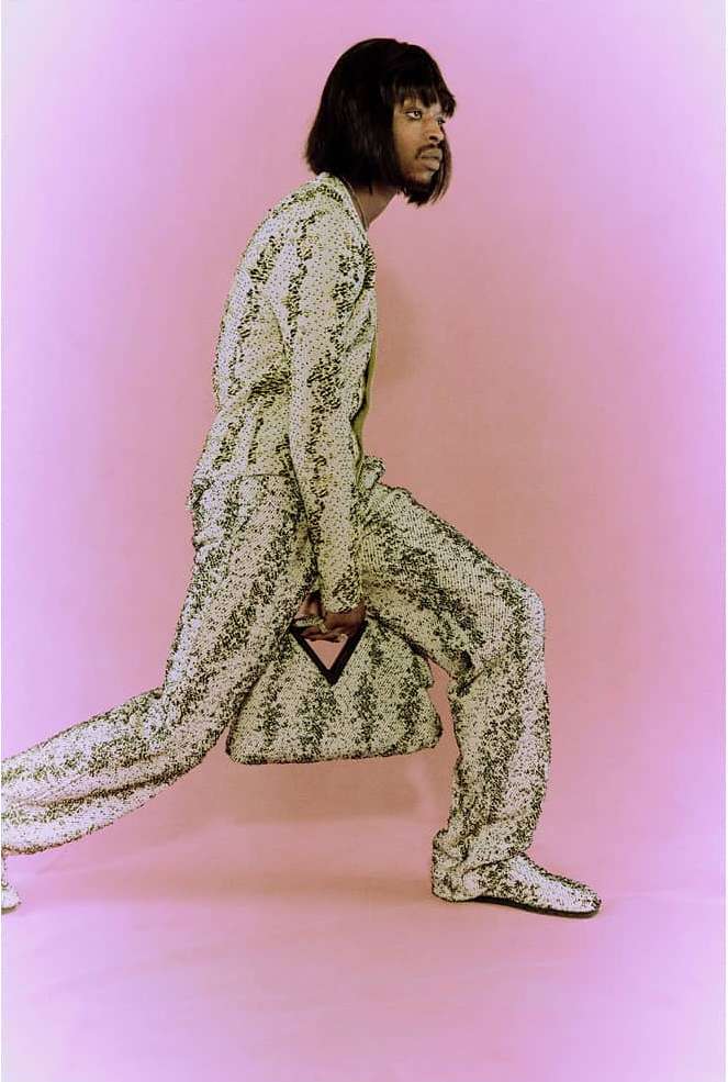 Model in patterned suit and matching handbag striding against a pink backdrop photographed by Amber Pinkerton