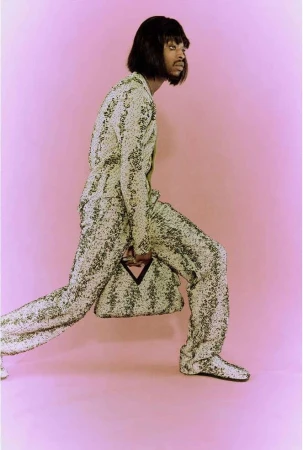 Model in patterned suit and matching handbag striding against a pink backdrop photographed by Amber Pinkerton
