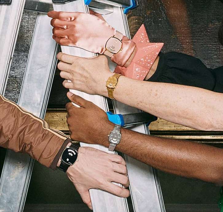 Close-up of four diverse arms wearing stylish watches while leaning against a ladder against an ornate Renaissance-style painting.
