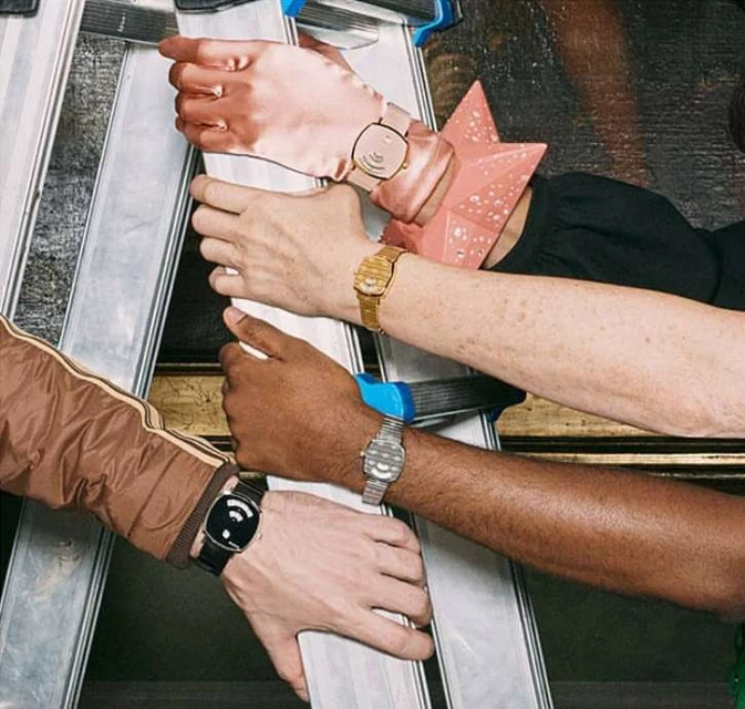 Close-up of four diverse arms wearing stylish watches while leaning against a ladder against an ornate Renaissance-style painting.