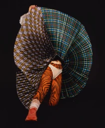 Model holding out a large pleated plaid skirt with tiger print leggings against a black background