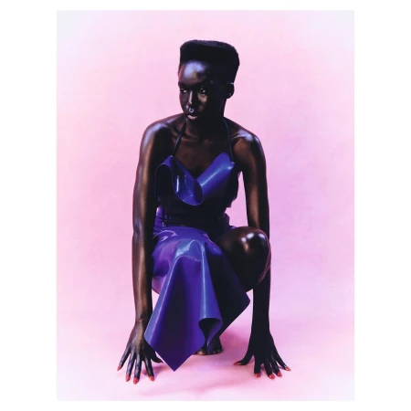 Portrait of a Black woman in a glossy purple dress squatting against a soft pink backdrop, photographed by Amber Pinkerton.
