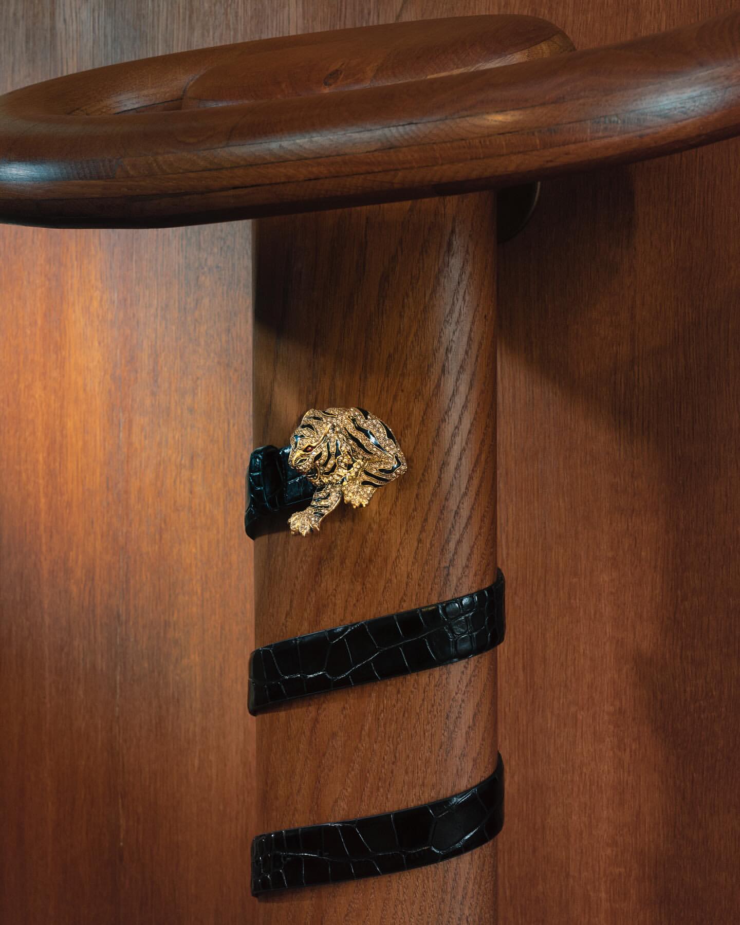 Close-up of wooden banister with a faux alligator skin accent band and jeweled tiger-shaped brooch on dark brown wood.