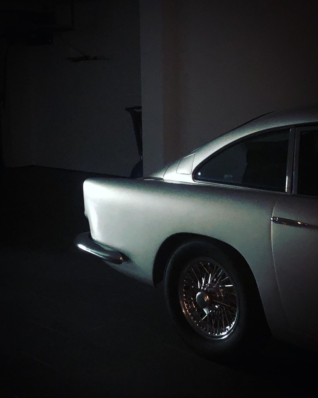 Silver vintage car parked indoors, showcasing its classic design, wire wheels, and sleek body in a softly lit environment.