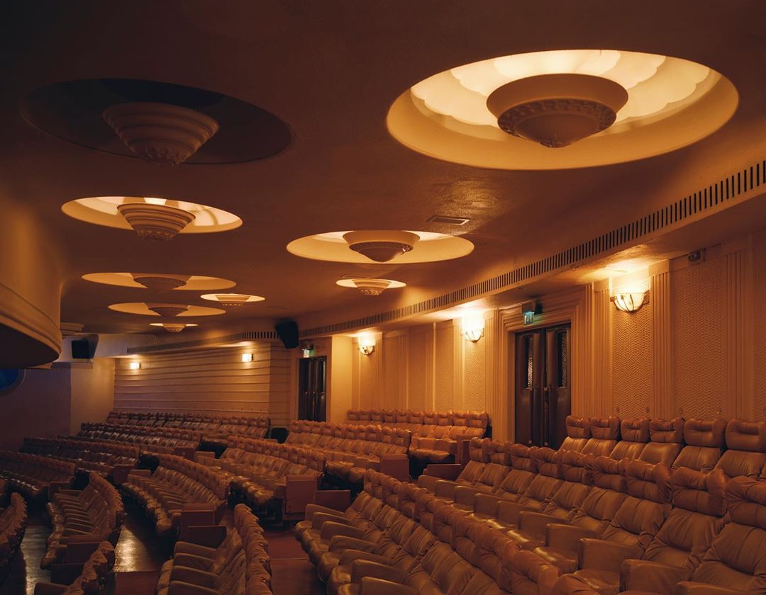 Interior view of a classic movie theater with rows of empty seats, ornate ceiling lights, and warm lighting creating a nostalgic atmosphere.