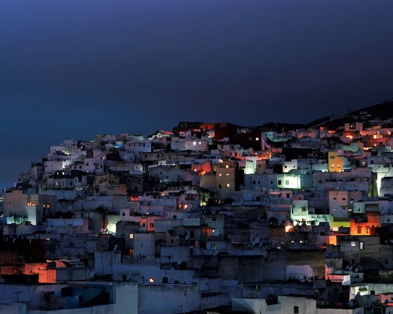 Night view of a densely packed urban landscape with illuminated buildings, showing a residential area at dusk with a clear sky.