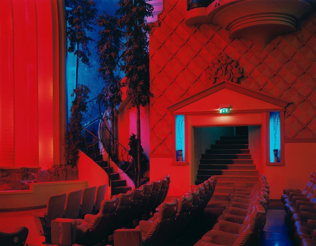 Indoor view of theater with rows of seats, staircase, and classical-style architecture lit with red and blue lighting.