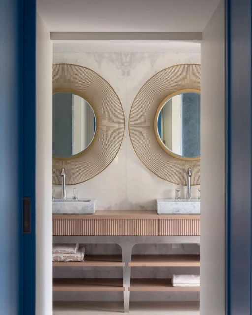 Modern bathroom interior featuring a double vanity with round mirrors, marble countertops, and open shelving for towels, illuminated by soft lighting.