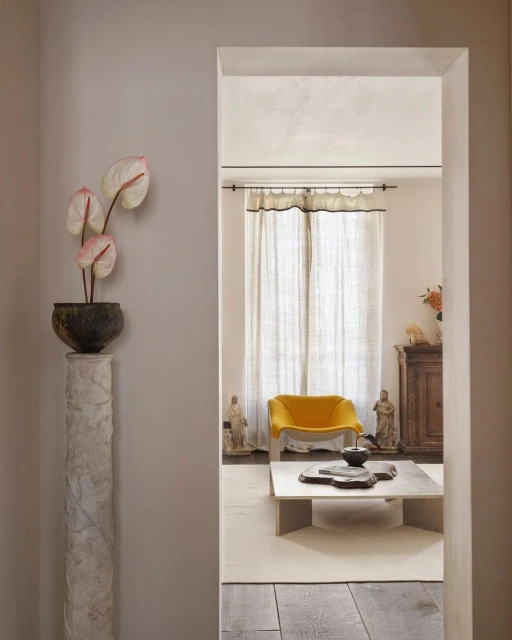 Interior view through an archway featuring a potted plant, a yellow chair, a stone coffee table, and decorative elements in a home.