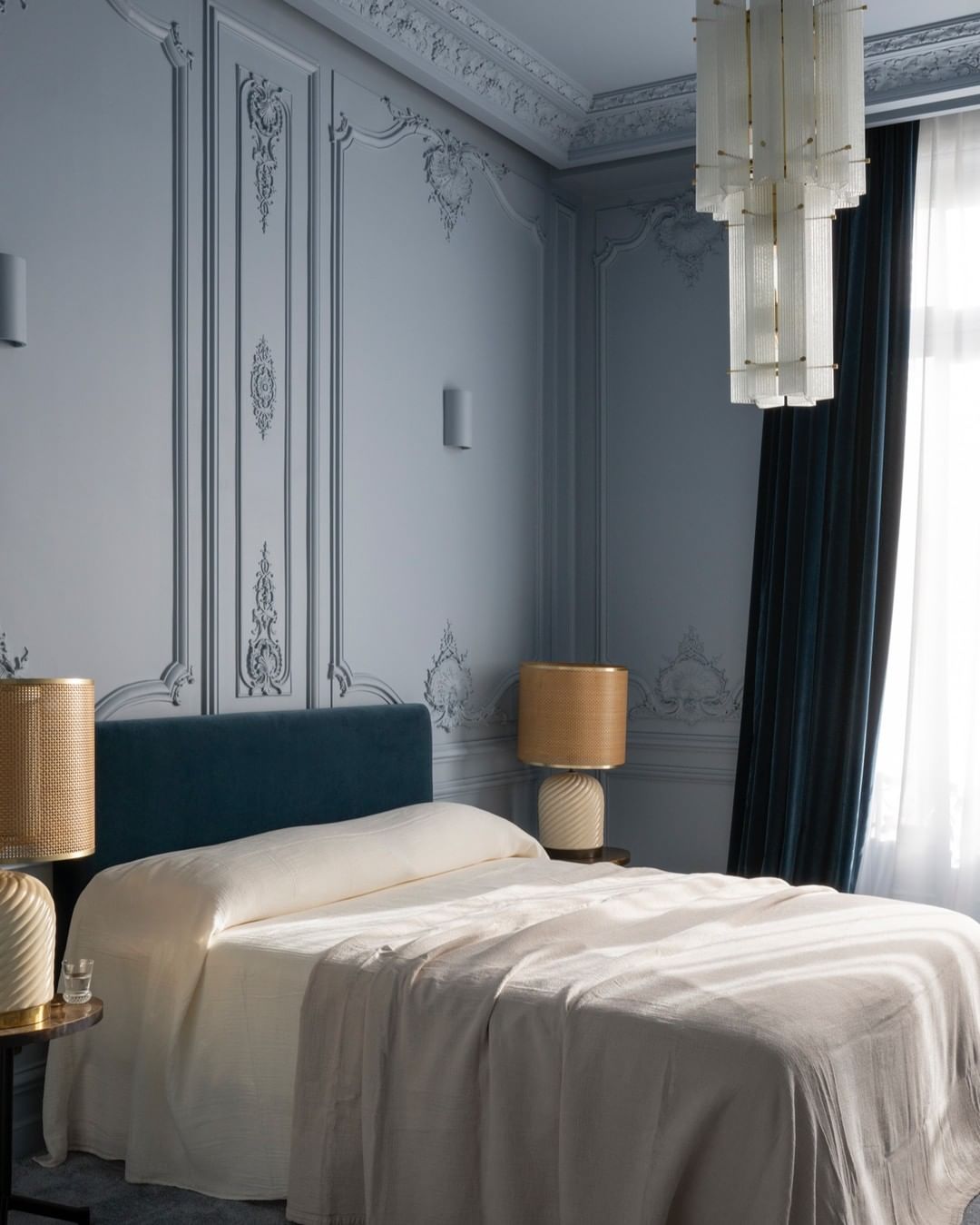 Interior of a classic-style bedroom featuring a large bed with a blue headboard, bedside tables with lamps, and decorative walls.