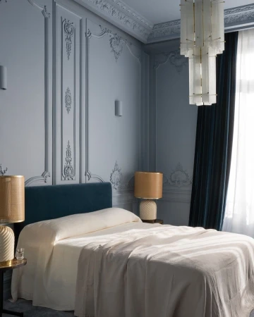 Interior of a classic-style bedroom featuring a large bed with a blue headboard, bedside tables with lamps, and decorative walls.