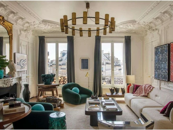 Living room interior with green armchairs, off-white sofa, ornate fireplace, and modern light fixture under decorative ceiling.