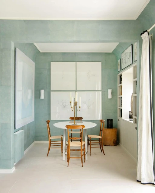 Interior of a dining room featuring a white round table, wooden chairs, and artwork on the wall in a room with light-green walls.