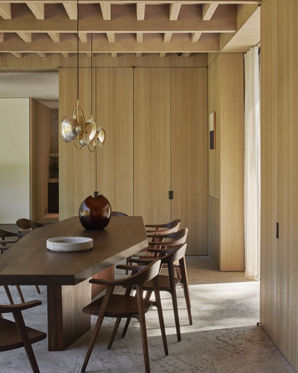 Dining room interior showcasing a dark wood table, chairs, pendant lighting, and neutral wood paneling in a modern architectural design.