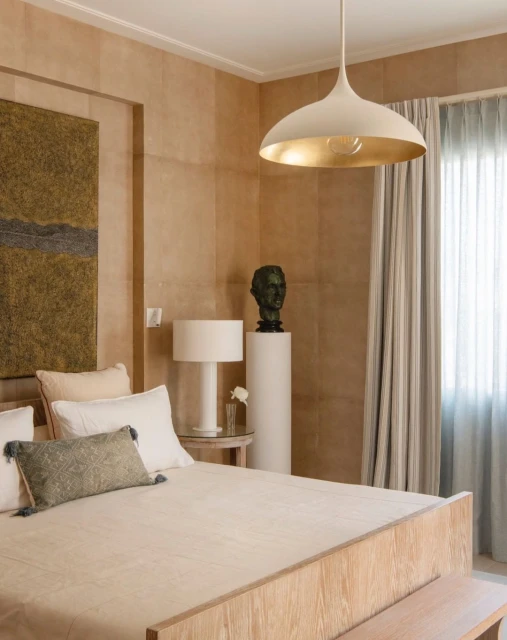 Bedroom interior with a wooden bed, neutral color palette, beige walls, and a modern pendant light fixture, creating a calm and inviting space.