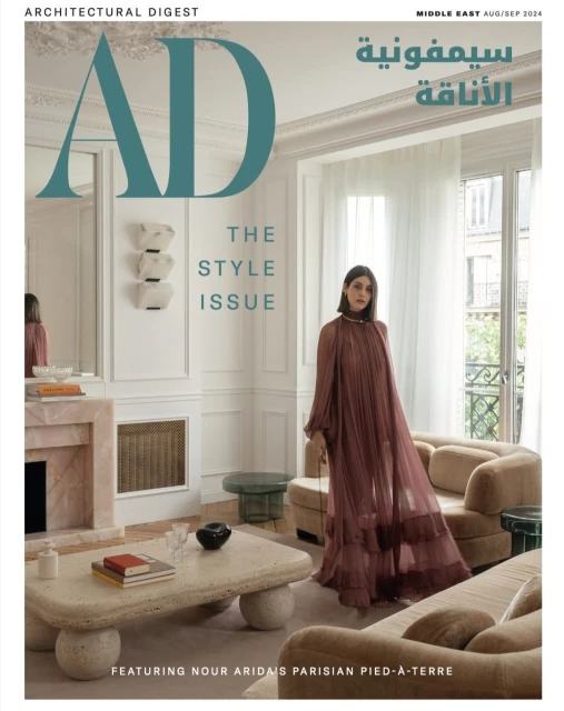 Magazine cover featuring a woman in a long dress standing in an elegant living room with a coffee table, sofa, and fireplace.