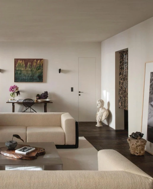 Living room interior with a neutral-toned sectional sofa, wooden coffee table, artwork, and decor in a bright, modern space.