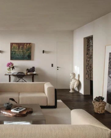 Living room interior with a neutral-toned sectional sofa, wooden coffee table, artwork, and decor in a bright, modern space.