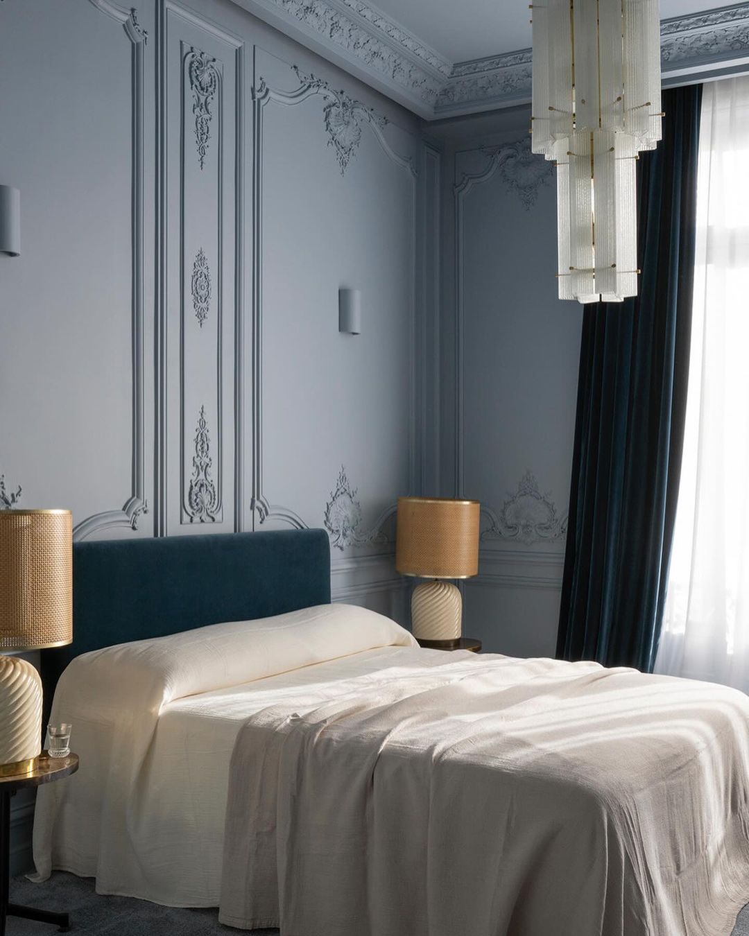 Luxurious bedroom interior with a bed, chandelier, and decorative moulding on blue walls, creating an elegant and cozy space.