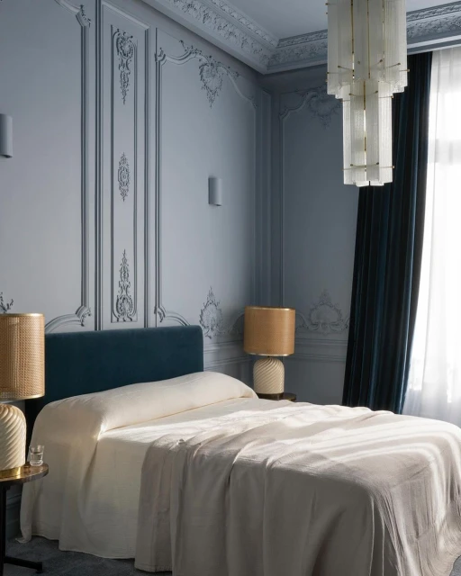 Luxurious bedroom interior with a bed, chandelier, and decorative moulding on blue walls, creating an elegant and cozy space.