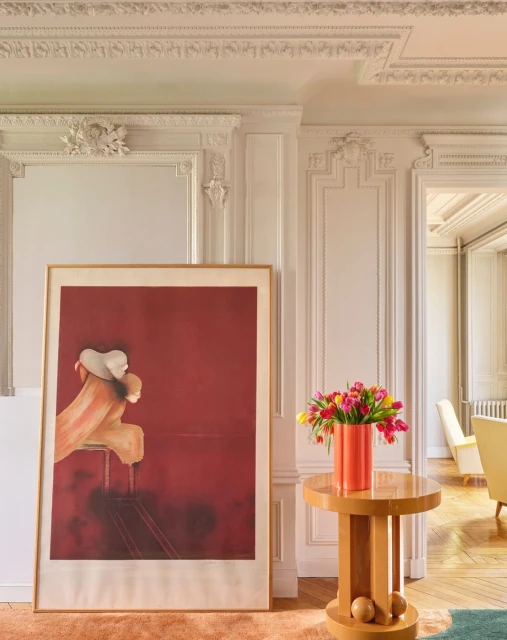 Living room interior featuring a painting, tulip flowers in a vase on a round table, decorative wall molding, and hardwood floors.