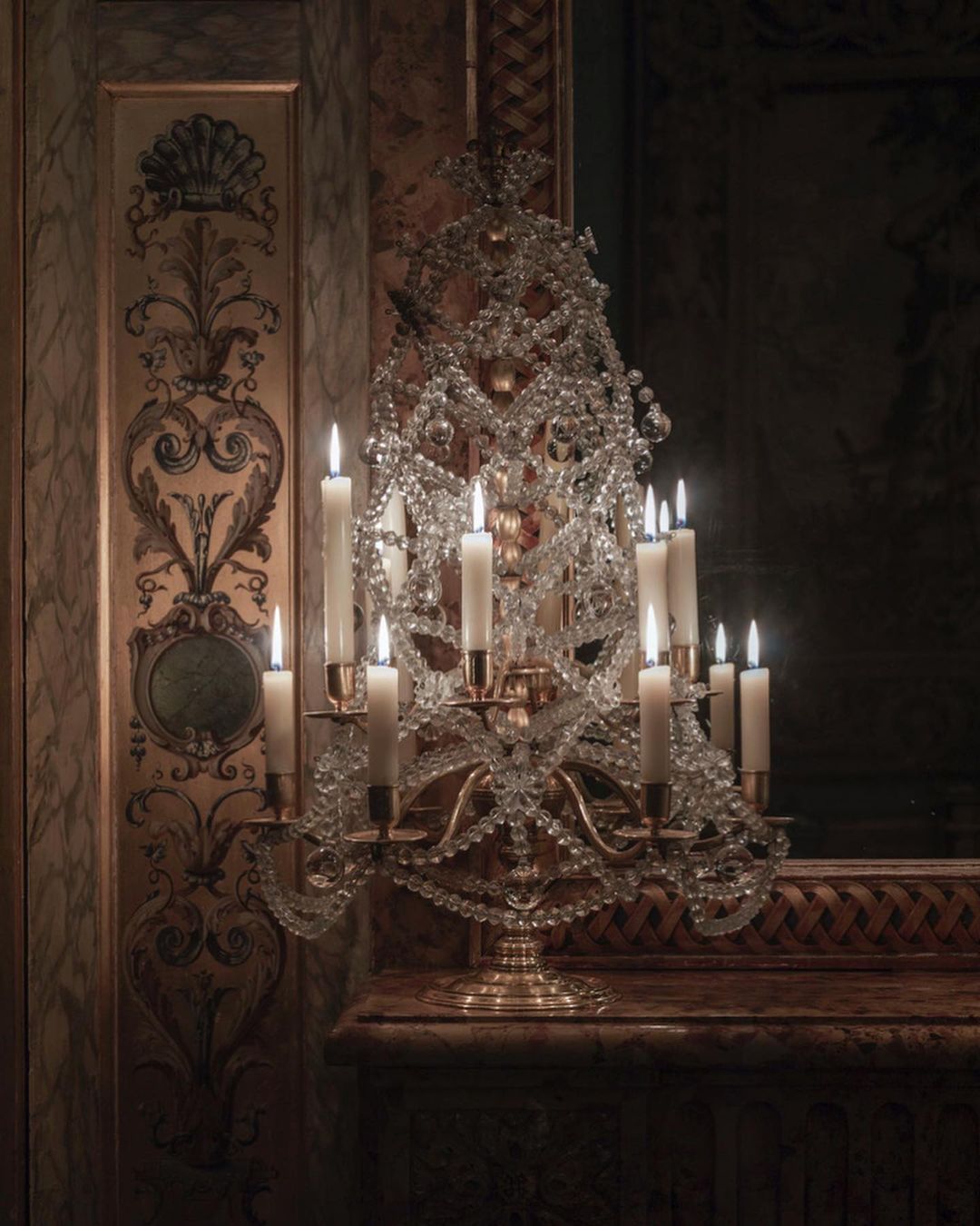 Crystal chandelier with lit candles on a marble surface against an ornate wall in a dimly lit indoor setting.