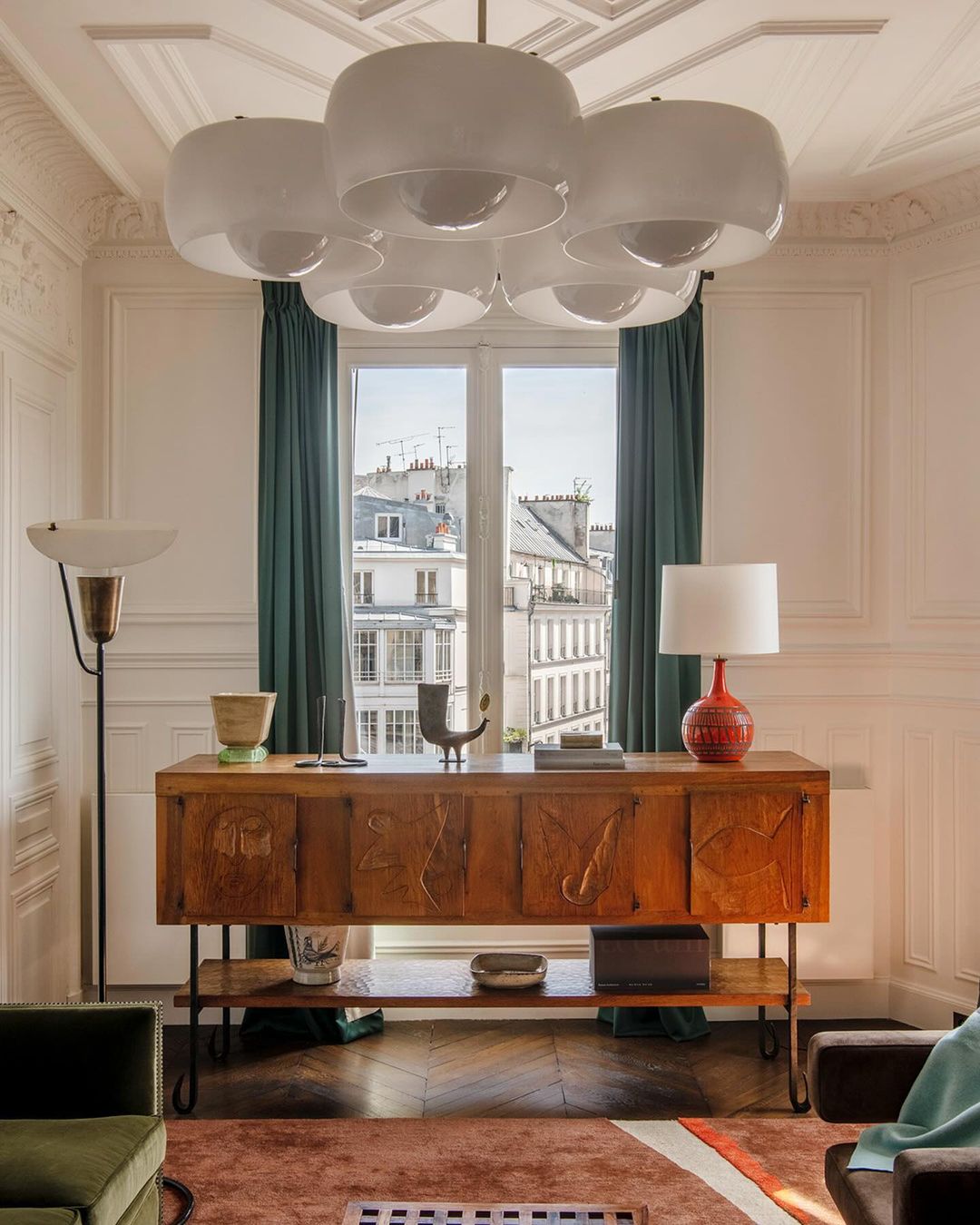 Living room interior featuring a wooden sideboard under a window, with a unique chandelier and various decorative objects adding to the decor.