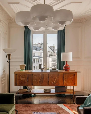Living room interior featuring a wooden sideboard under a window, with a unique chandelier and various decorative objects adding to the decor.
