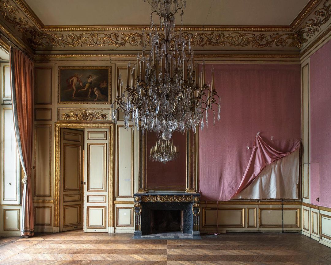 Ornate vintage room featuring a chandelier, fireplace, and decorative walls with a parquet floor in a distressed interior setting.