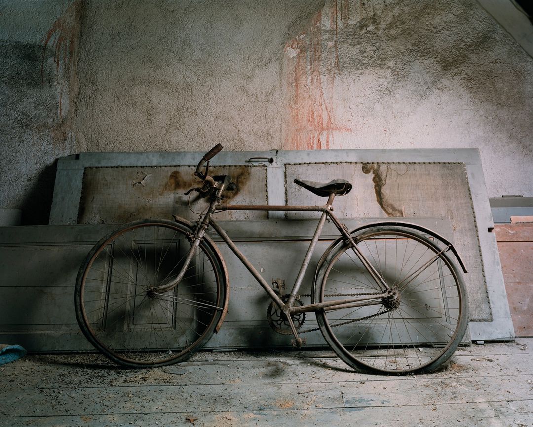 Vintage bicycle leaning against a textured wall and a weathered door in an indoor setting, creating a nostalgic and rustic atmosphere.