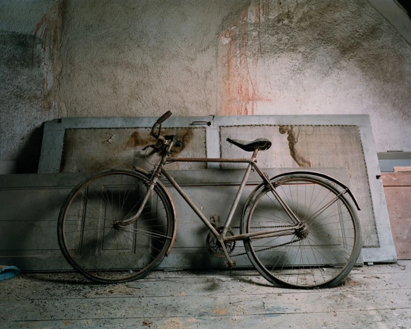 Vintage bicycle leaning against a textured wall and a weathered door in an indoor setting, creating a nostalgic and rustic atmosphere.