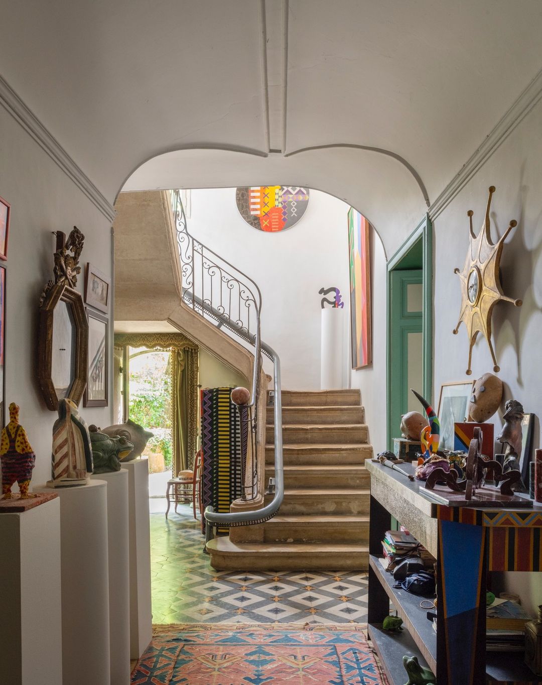 View of an interior hallway and staircase, featuring decorative objects, artwork, and patterned flooring, creating a vibrant and artistic home space.